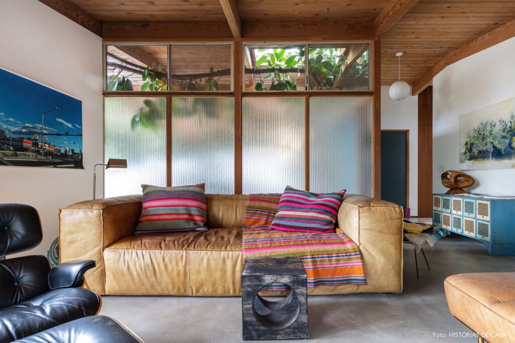 SALA COM SOFÁ EM LINHAS RETAS DE COURO, MANTA E ALMOFADA COLORIDAS