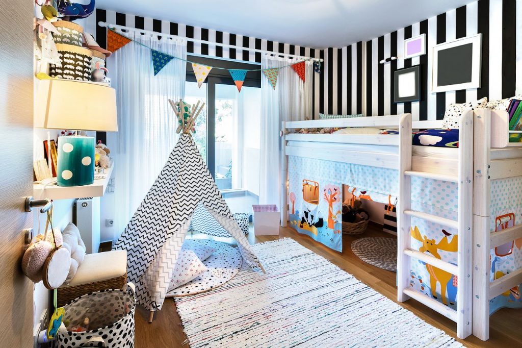 QUARTO DE BEBE COM PAREDE EM LISTRAS EM BRANCO E PRETO, CABANA E BANDEIROLAS
