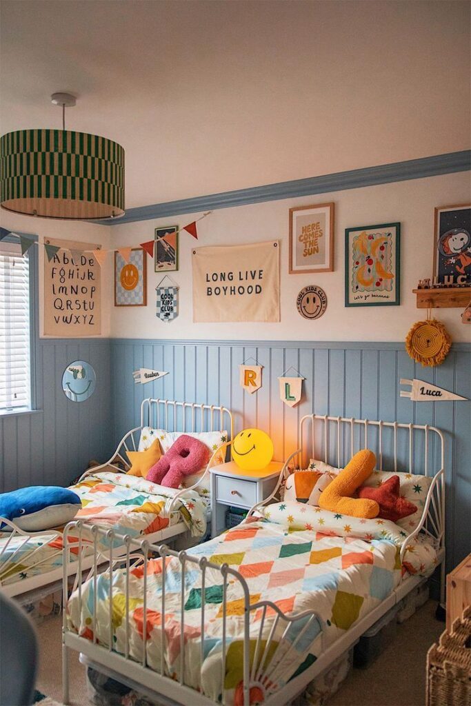 QUARTO DE BEBE COM MEIA PAREDE AZUL, MOLDURA DE GESSO NO MESMO TOM, COLCHA DE CAMA COLORIA E CAMAS EM ESTILO VINTAGE