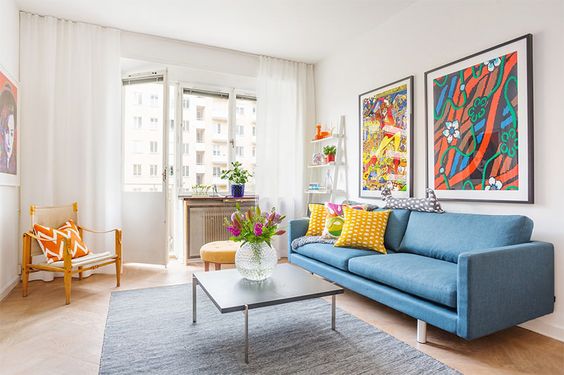 SALA COM SOFÁ AZUL, QUADROS E ALMOFADAS COLORIDOS